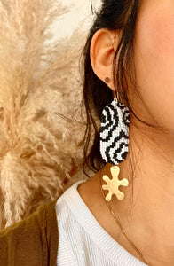 female wearing woven earrings with black and white beads in a wave formation with a hanging curved brass piece